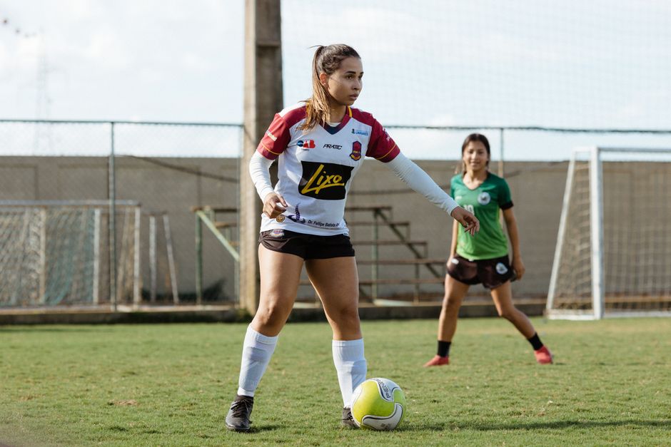 Two teenage girls engaged in a soccer game on an outdoor field, wearing sportswear.
