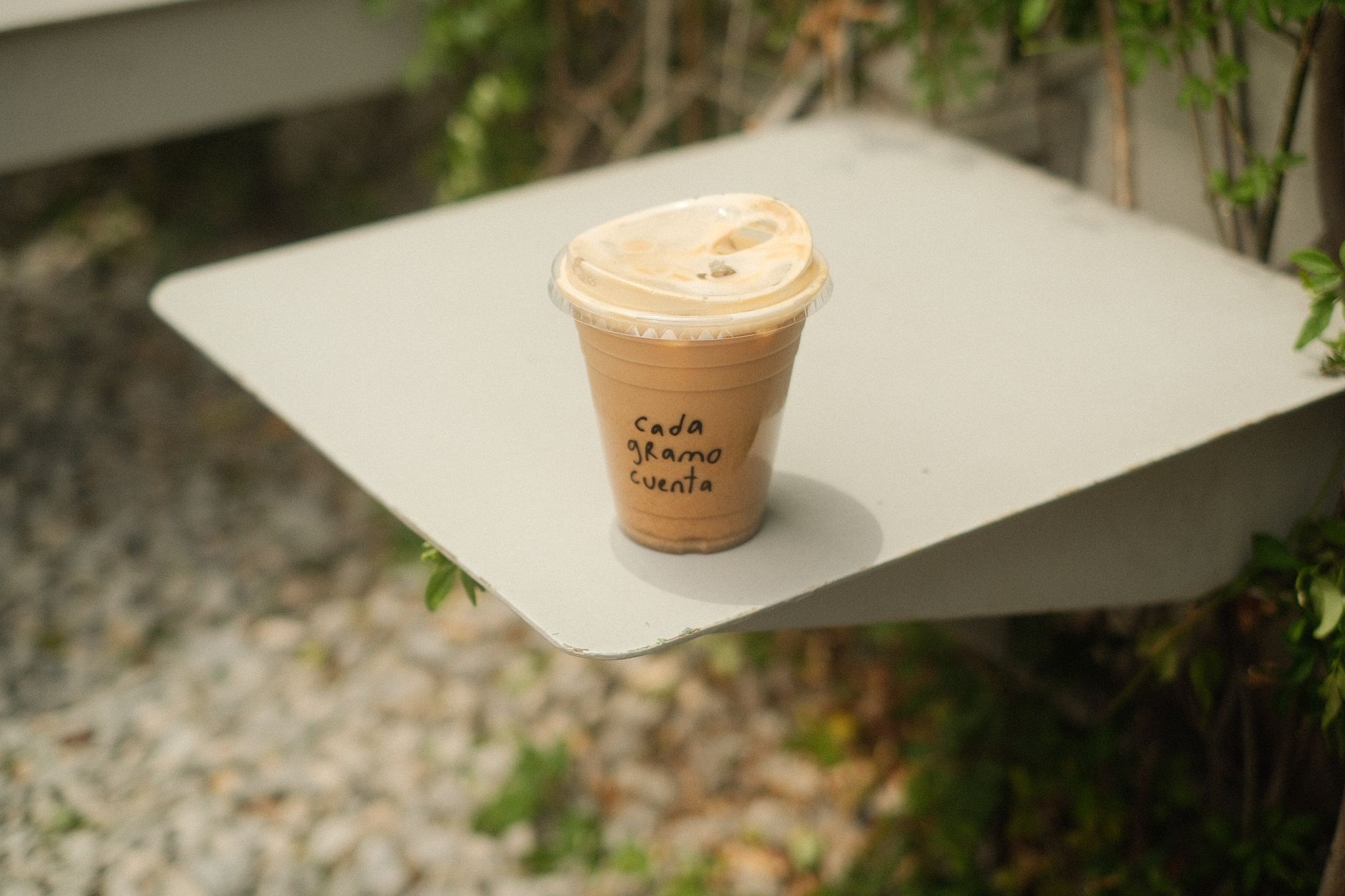 Iced coffee on a table outdoors with text 'cada gramo cuenta', evoking motivation.