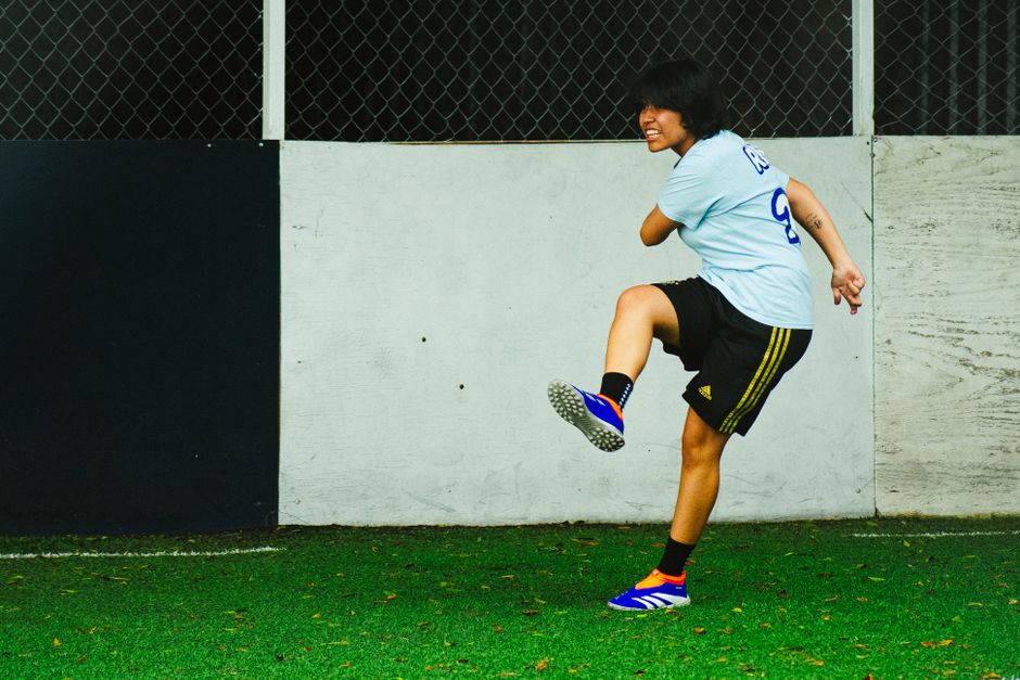 Dynamic shot of a woman footballer performing a powerful kick on an indoor sports court.