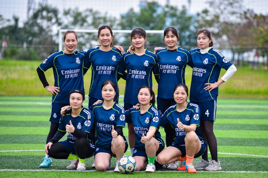 A women's football team poses for a group photo on a green field in Hanoi, Vietnam.