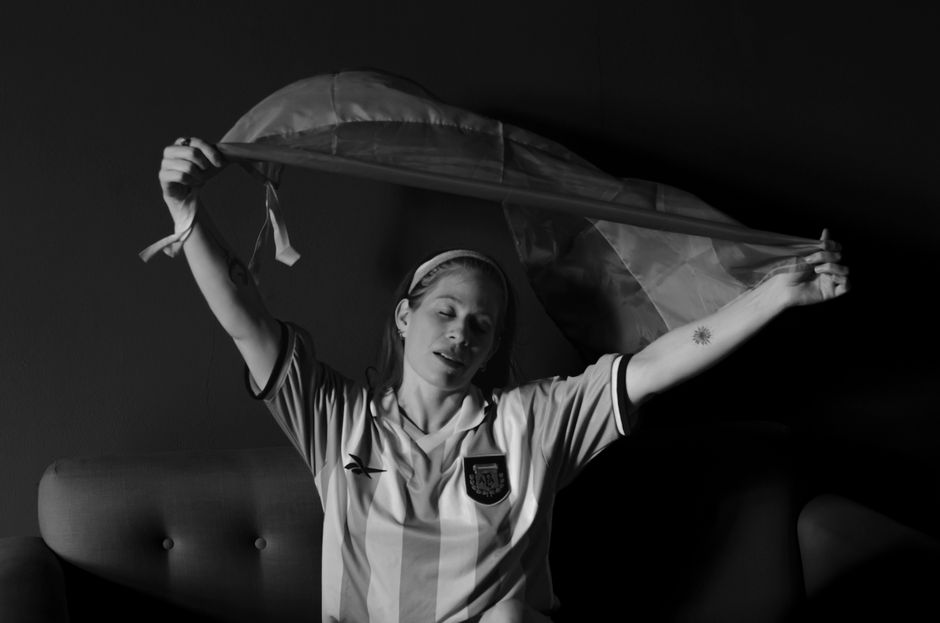 Black and white portrait of a football fan with the Argentinian flag indoors.