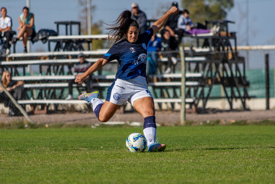 A female footballer in action, kicking the ball during a competitive match outdoors.