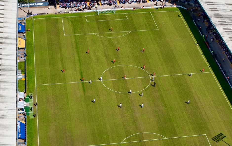 Aerial view of a football match in a sunlit stadium in Manchester.