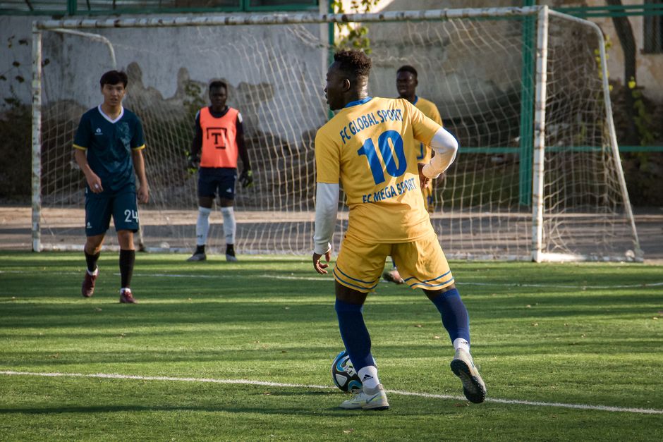 Players engage in a soccer match in Almaty, Kazakhstan, showcasing team sportsmanship on a sunny day.